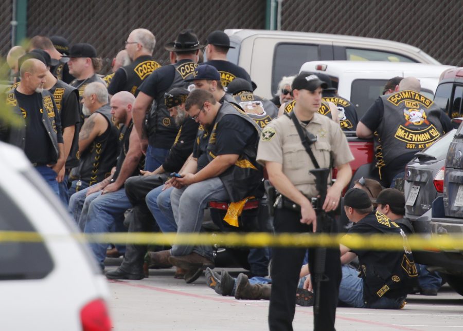 FILE - In this May 17, 2015 file photo, a McLennan County deputy stands guard near a group of bikers in the parking lot of a Twin Peaks restaurant in Waco, Texas.  The prevailing images of protests in Baltimore and Ferguson, Missouri, over police killings of black men were of police in riot gear, handcuffed protesters, tear gas and mass arrests. The main images of a fatal gun battle between armed bikers and police in Waco, Texas, also showed mass arrests _ carried out by nonchalant-looking officers sitting around calm bikers on cell phones.  (Rod Aydelotte/Waco Tribune-Herald via AP)