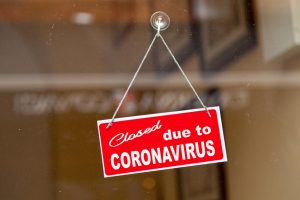 Red sign hanging at the glass door of a shop saying Closed due to coronavirus.