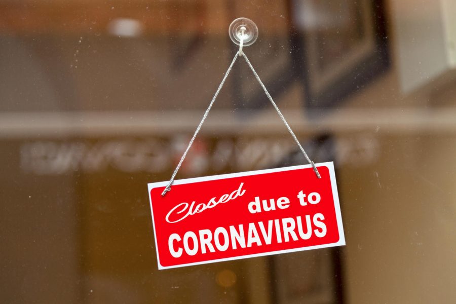 Red sign hanging at the glass door of a shop saying Closed due to coronavirus.