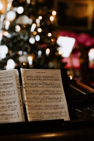 Holiday music is displayed on a piano in front of a Christmas tree. 