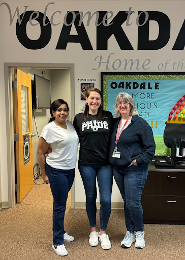 Mrs. Jackson, Mrs. Moore, and Mrs. Bratburd (left to right) pose for a photo in front of the bulletin board in the front office. 
