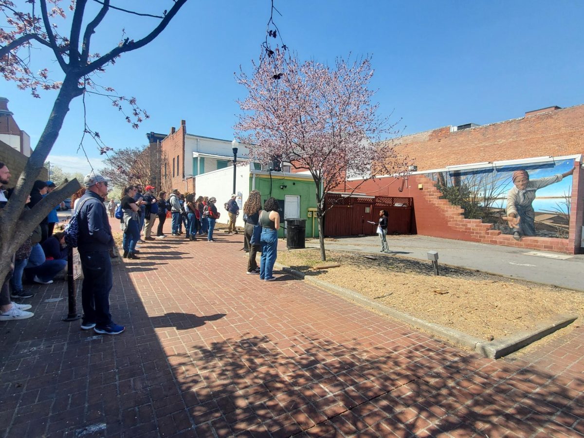 Volunteer, Kessia Donfack Djoko, discusses the significance of the "Take My Hand" mural outside the Harriet Tubman Museum Center in downtown Cambridge, Maryland.